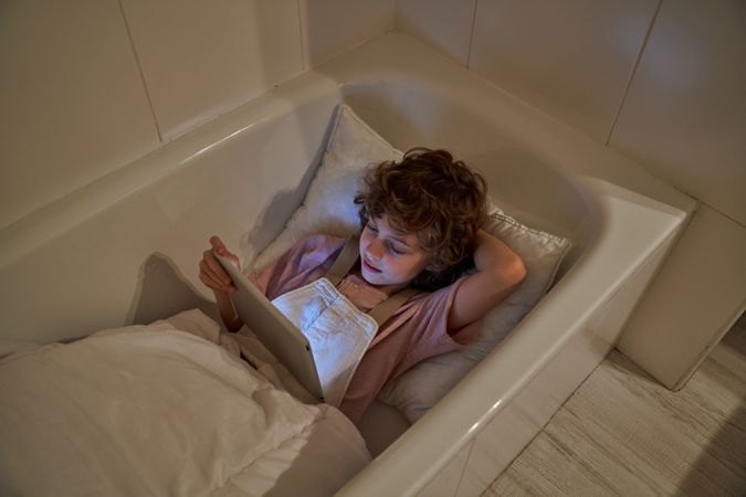 Boy lying in bathtub with tablet