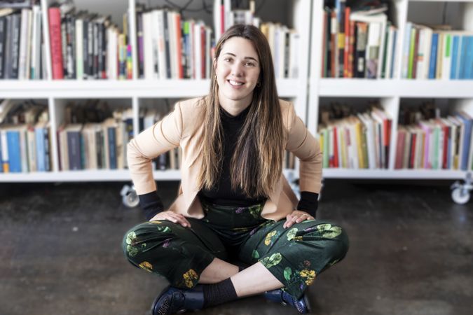 Portrait of a smiling woman sitting cross legged in front of book shelf
