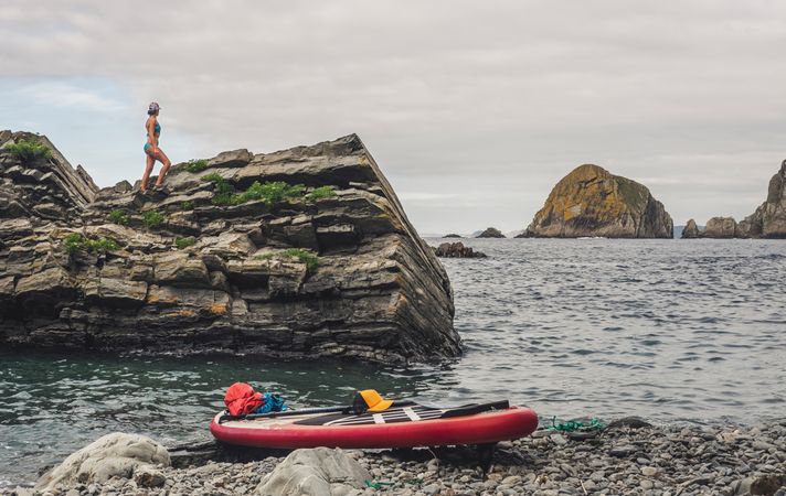 Woman on rough cliff near paddle board