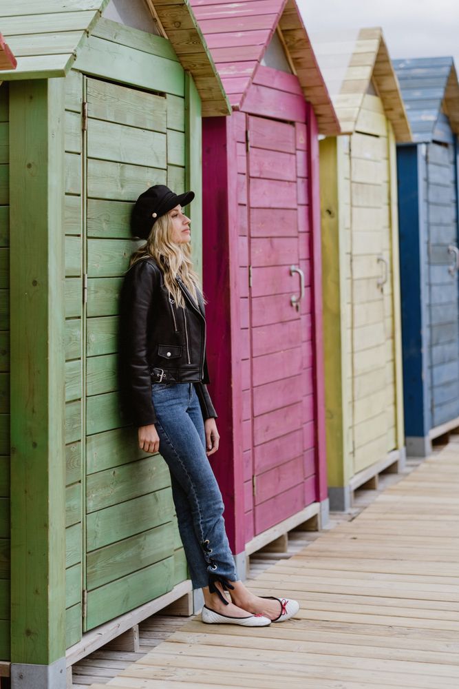 Stylish woman smiling and leaning on bright wooden cabins on beach