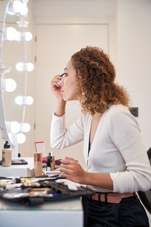 Young woman applying eye makeup sitting in front of mirror