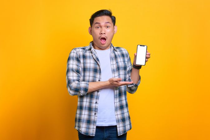 Surprised Asian male showing blank screen of smart phone in studio shoot