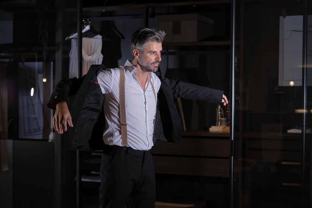 Man in suit standing near glass wall and putting on jacke