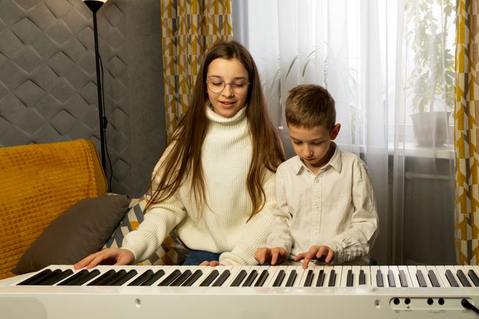 Girl and boy play piano together in cozy home setting.