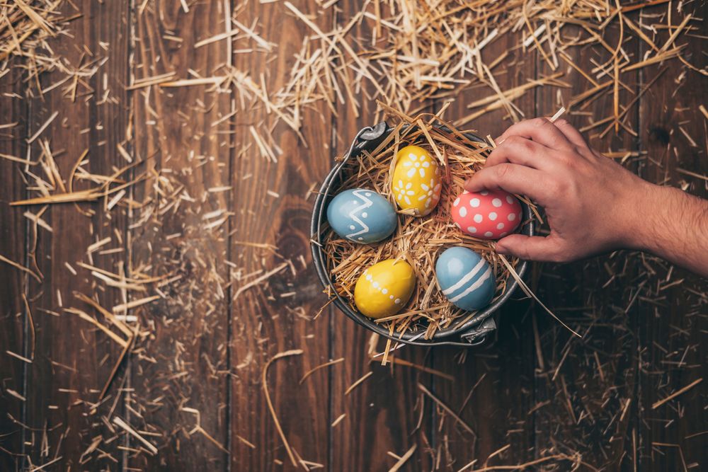 Hand placed Easter eggs on bucket with straw