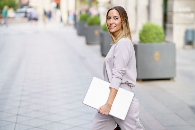 Content woman in grey walking outside with laptop