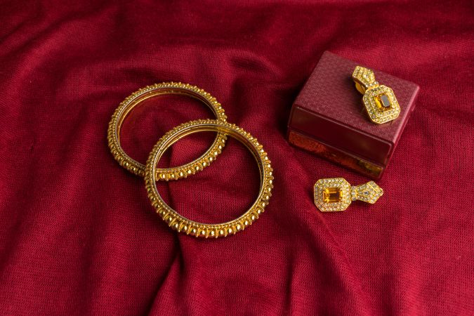 Beautiful shiny golden bangles and diamond studded traditional earrings on a red velvet background