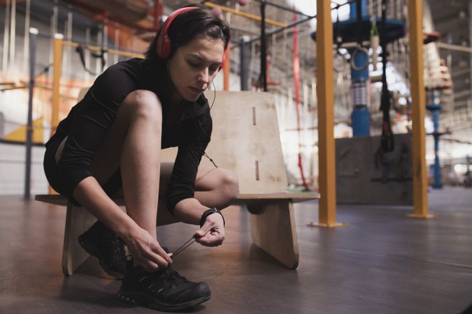 Smiling woman with headphones lacing shoe in gym