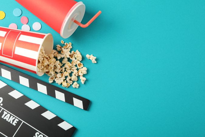 Flat lay. Drink, bucket with popcorn, clapperboard and confetti on color background, copy space