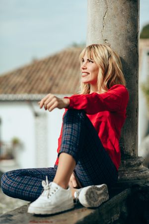 Relaxed blond woman sitting on cement stoop with pillar in Spanish town