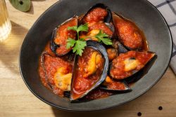 Cooked plate of mussels in tomato sauce on table