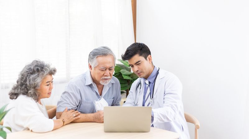 Doctor using computer discussing test result with mature Asian couple