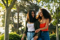 two young women, a couple, walking holding hands in a park