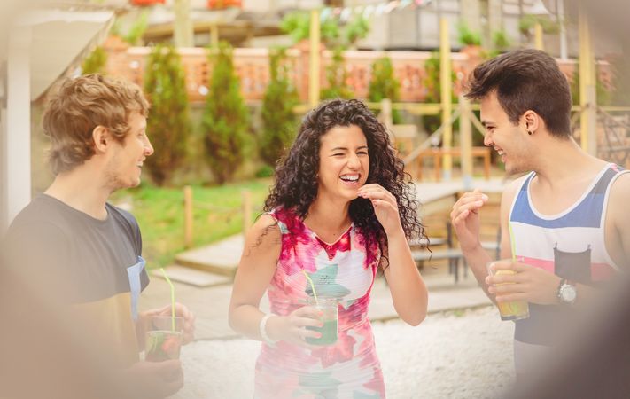 Laughing friends having cocktails in garden seem through fence