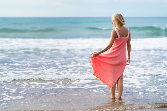 Back of older woman standing on the beach facing the ocean, copy space