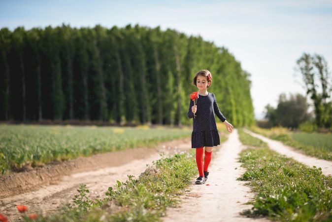 Girl walking on path with red flowers in her hand
