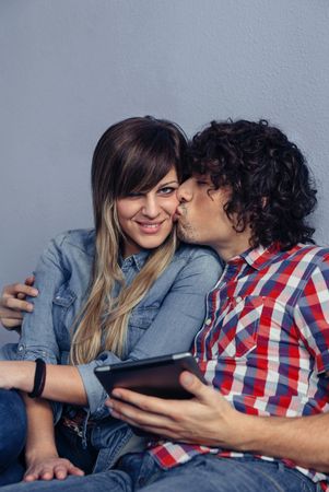 Man kissing woman and holding tablet