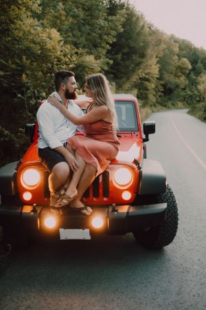 Loving couple sitting on car on road near forest