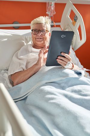Cheerful older woman with tablet on hospital bed