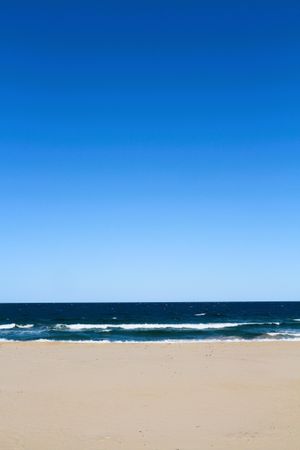 Calm beach under a clear blue sky with gentle waves lapping on the shore during a sunny day