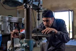 Focused mechanic working with vertical drill in garage