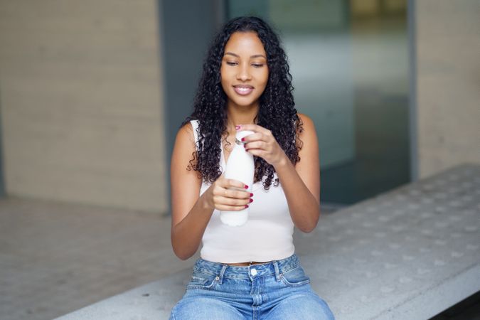 A Young Woman is Enjoying a Healthy and Refreshing Drink While Sitting Outdoors Happily