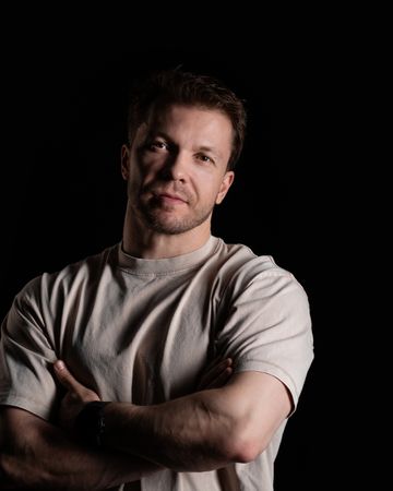 Man with arms crossed wearing beige t-shirt, confident pose.