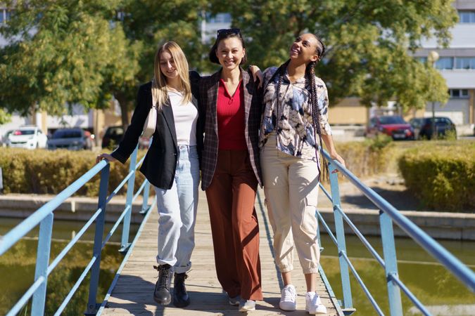 Three smiling women on pedestrian bridge on summer’s day