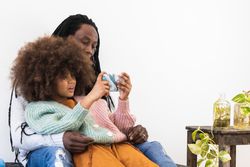 Black man embracing daughter while watching smartphone together