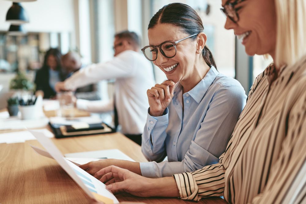 Two woman smiling and working together on a chart