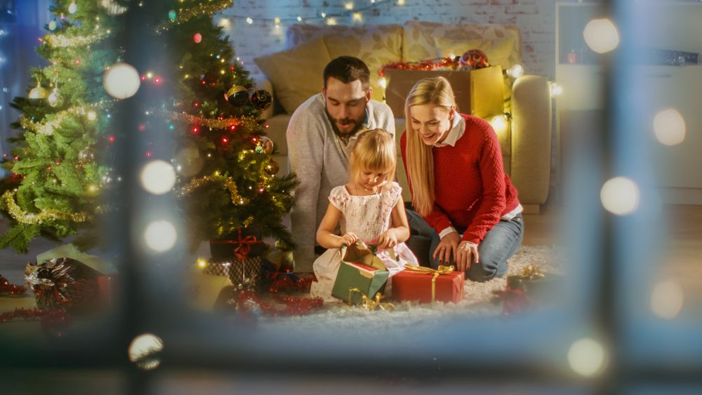 Looking Through Snowy Window at Happy Father, Mother and Daughter Sitting Under Christmas Tree.