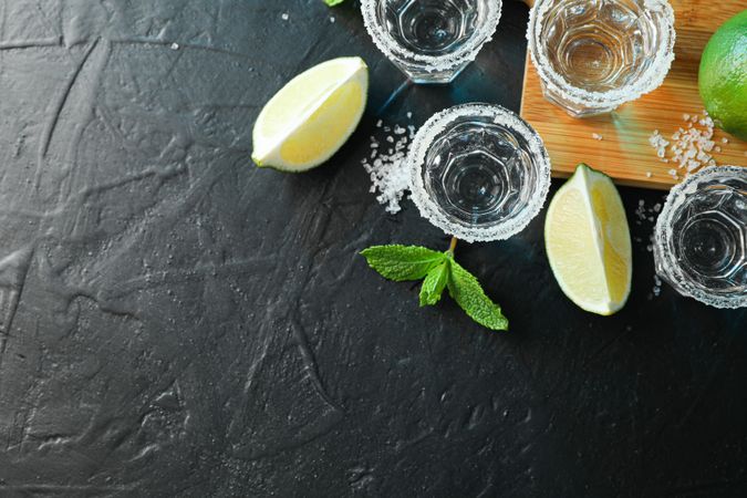 Tequila shots with salt, lime slices and mint on dark table