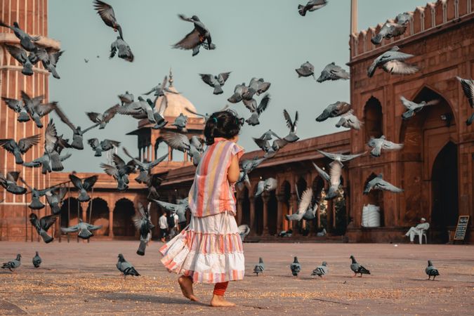 Back view of a girl playing in a courtyard surrounded by pigeons