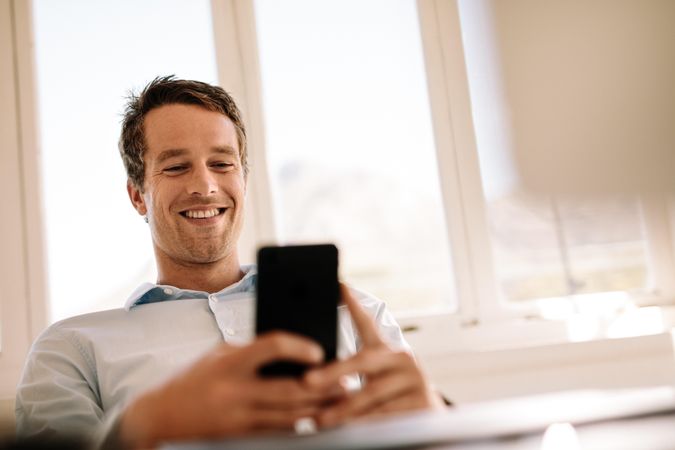 Low angle shot of male smiling at mobile phone