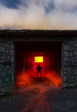 Dark person in garage in redness and cloudy sky