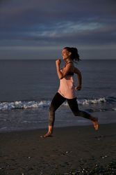 Content Hispanic woman running on sandy shore