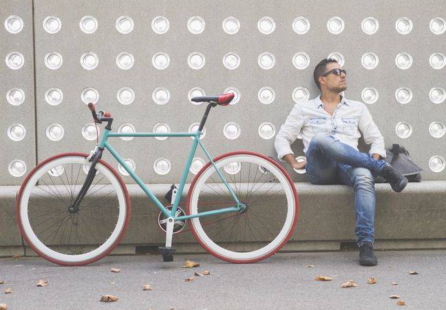 Male looking away while sitting with bike parked in front of patterned cement wall