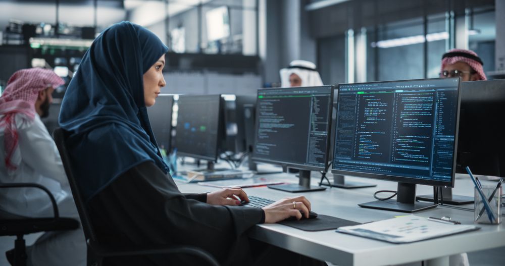Young Middle Eastern Specialist in a Hijab Writing Advanced Software Code on a Desktop Computer
