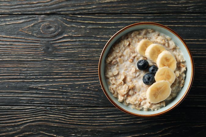 Bowl with oatmeal porridge and fruits on wooden background