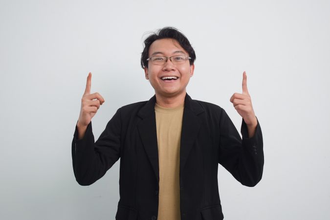 Joyful Asian businessman with suit and casual shirt pointing up