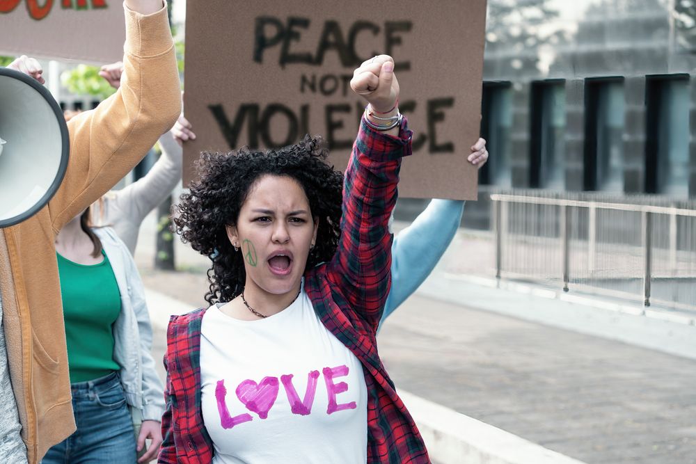 A fervent young woman with curly hair raises her fist in a powerful gesture