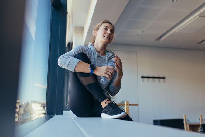 Woman relaxing after workout sitting beside a window in a pilates gym