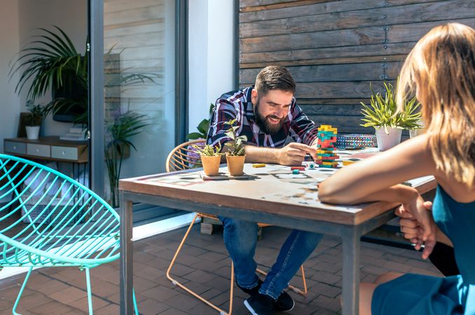 Bearded man catching game piece with colleague on terrace