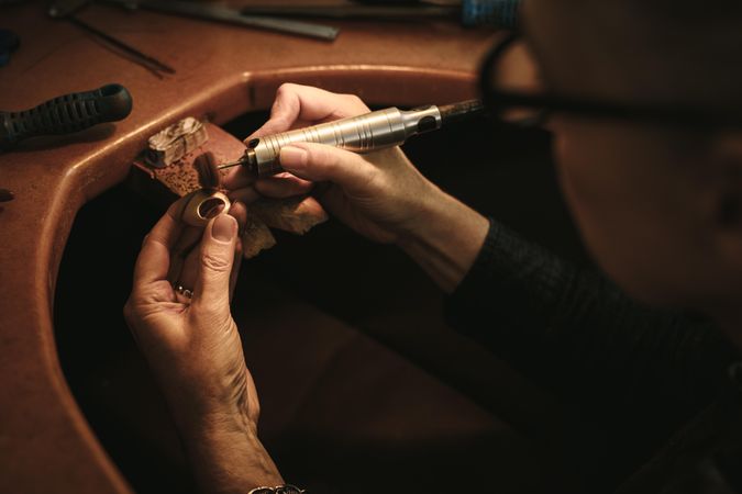 Hands of  woman goldsmith polishing off the sharp edges on a ring at her workbench