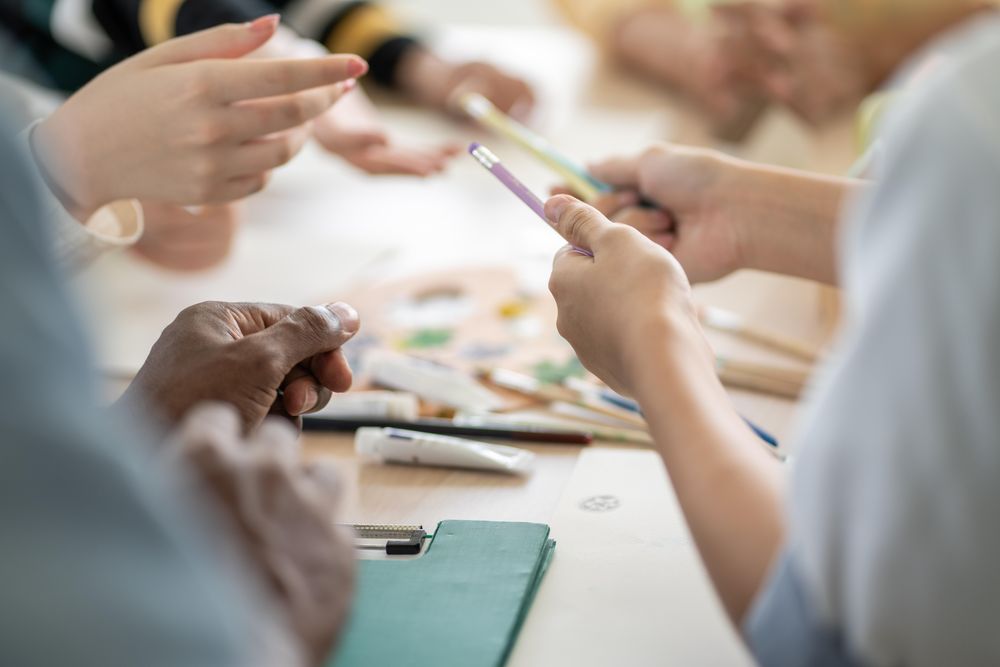 Students hands using paint and brushes on classroom table
