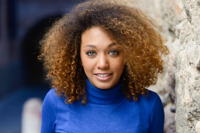 Woman with curly hair smiling outside in city