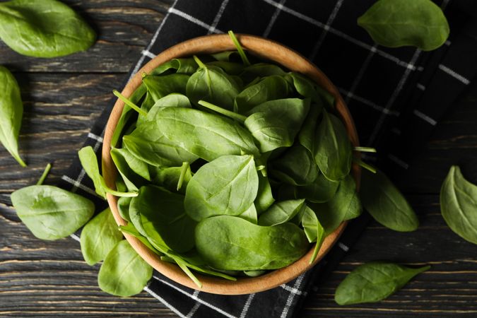 Wooden bowl with spinach and napkin on wooden background