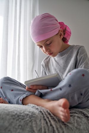 Focused boy symbolic pink scarf writing in notepad