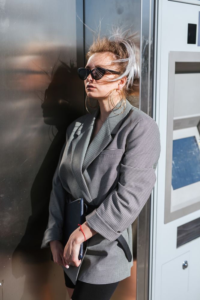 Stylish woman in black sunglasses leaning on metal wall