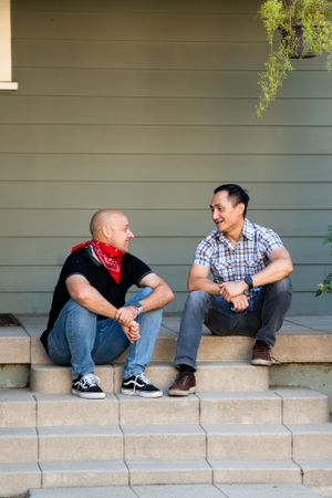Two men talking and sitting on a front porch in the afternoon